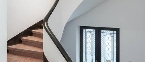 A spiral staircase with a white handrail and beige steps, leading to a door with a black frame and decorative glass panels.