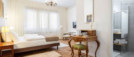 A hotel room with a bed, a desk, a chair, a mirror, and a shower area.