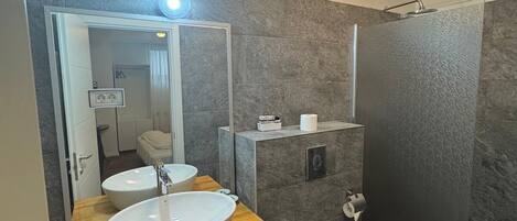 A modern bathroom with a large mirror, two sinks, a toilet, and a shower.