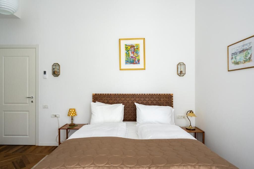 A neatly arranged bedroom with a large bed, two bedside tables with lamps, a framed artwork above the bed, and a door to the left.