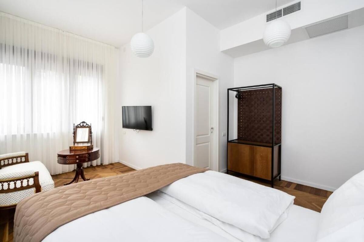 A modern hotel room with a large bed, a bedside table, a mirror, a TV, and a wardrobe.
