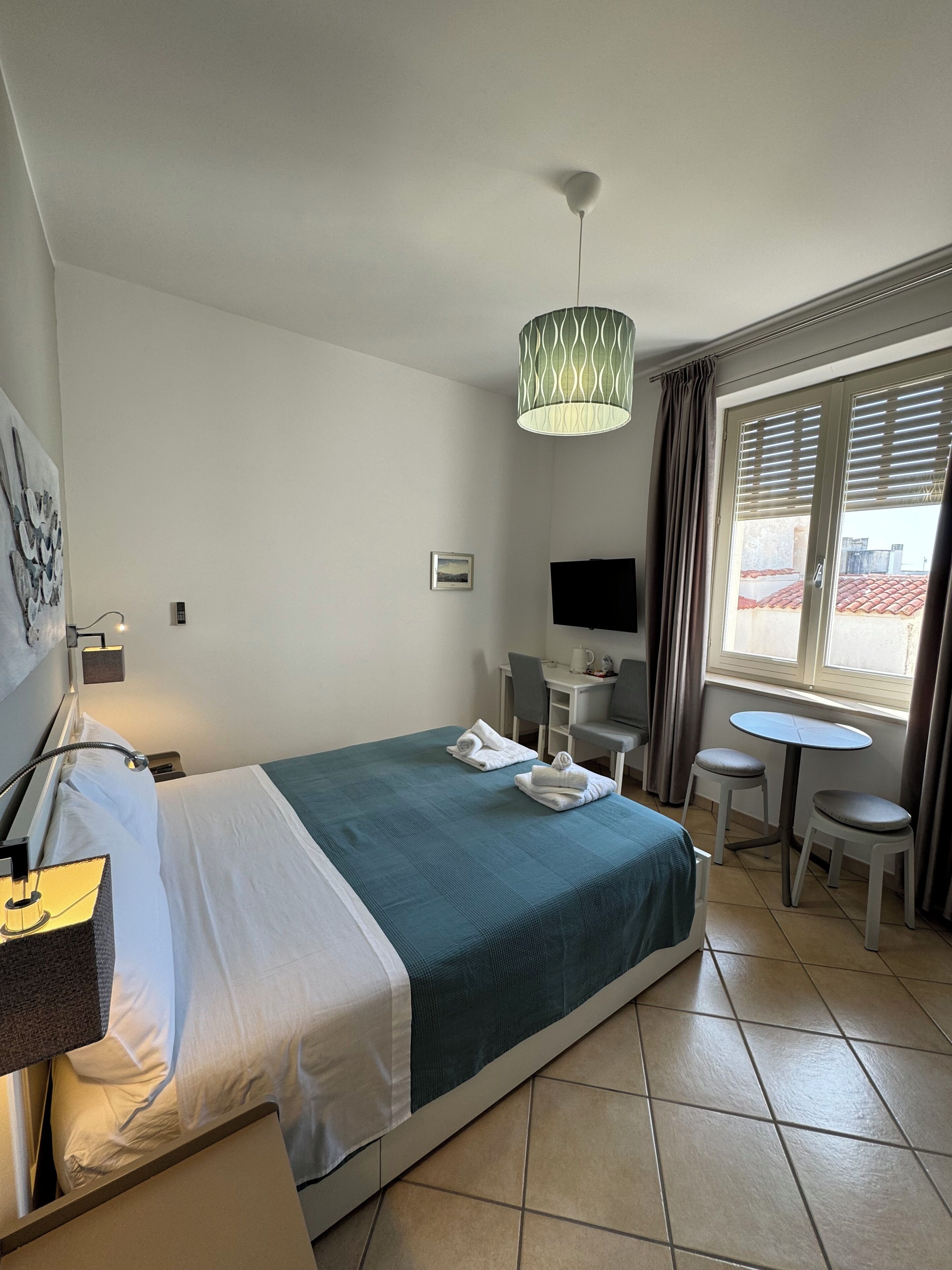 Una habitación de hotel con cama, escritorio, silla, televisión y ventana con cortinas.
