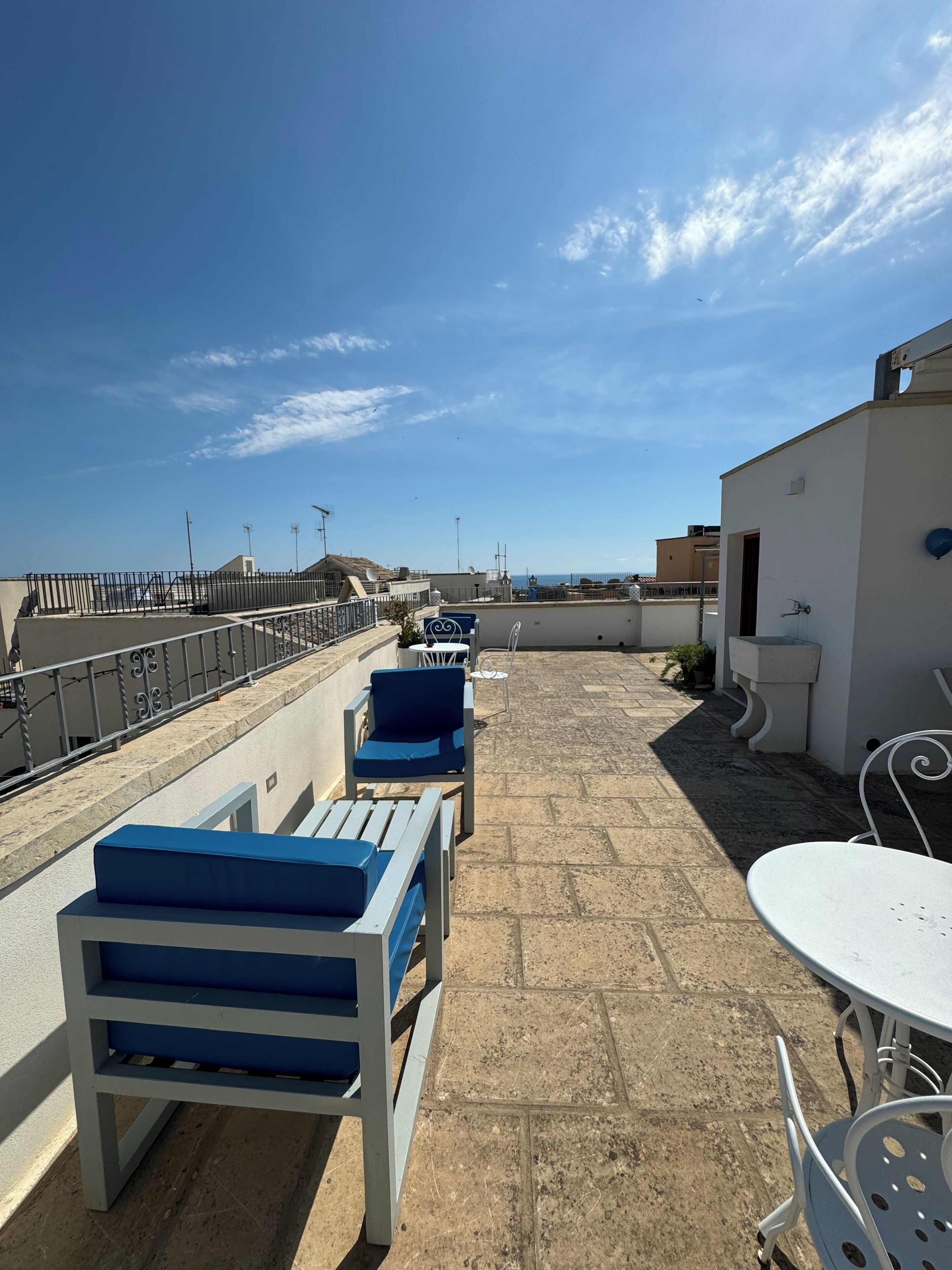 En takterrass med blå och vita loungestolar, ett vitt bord och utsikt över havet.