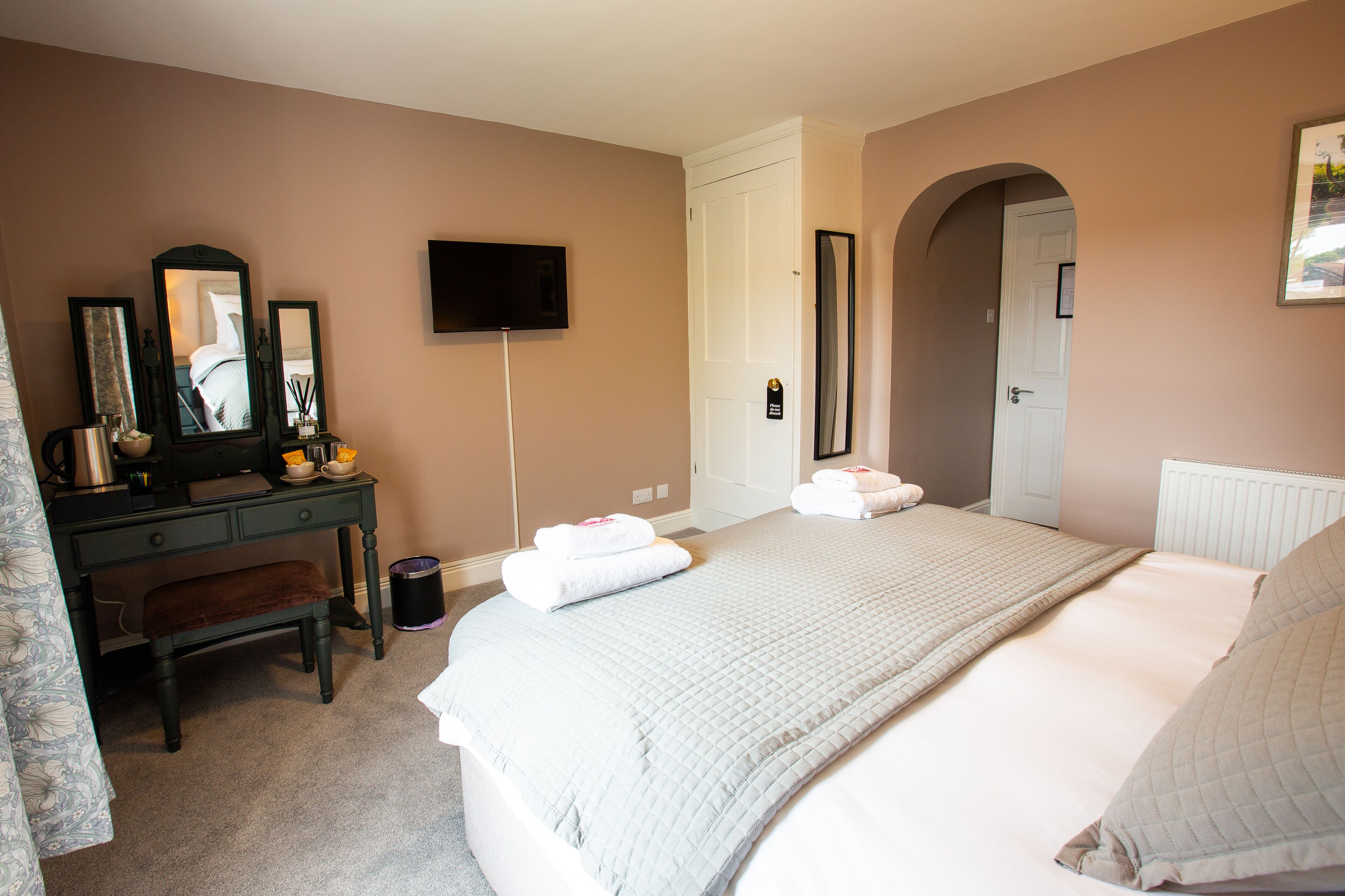 A bedroom with a bed, a dresser, a mirror, a television, and a door leading to another room.