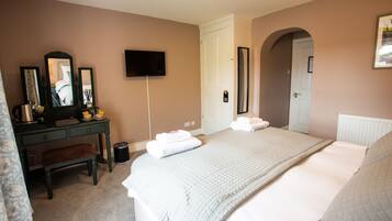 A bedroom with a bed, a dresser, a mirror, a television, and a door leading to another room.
