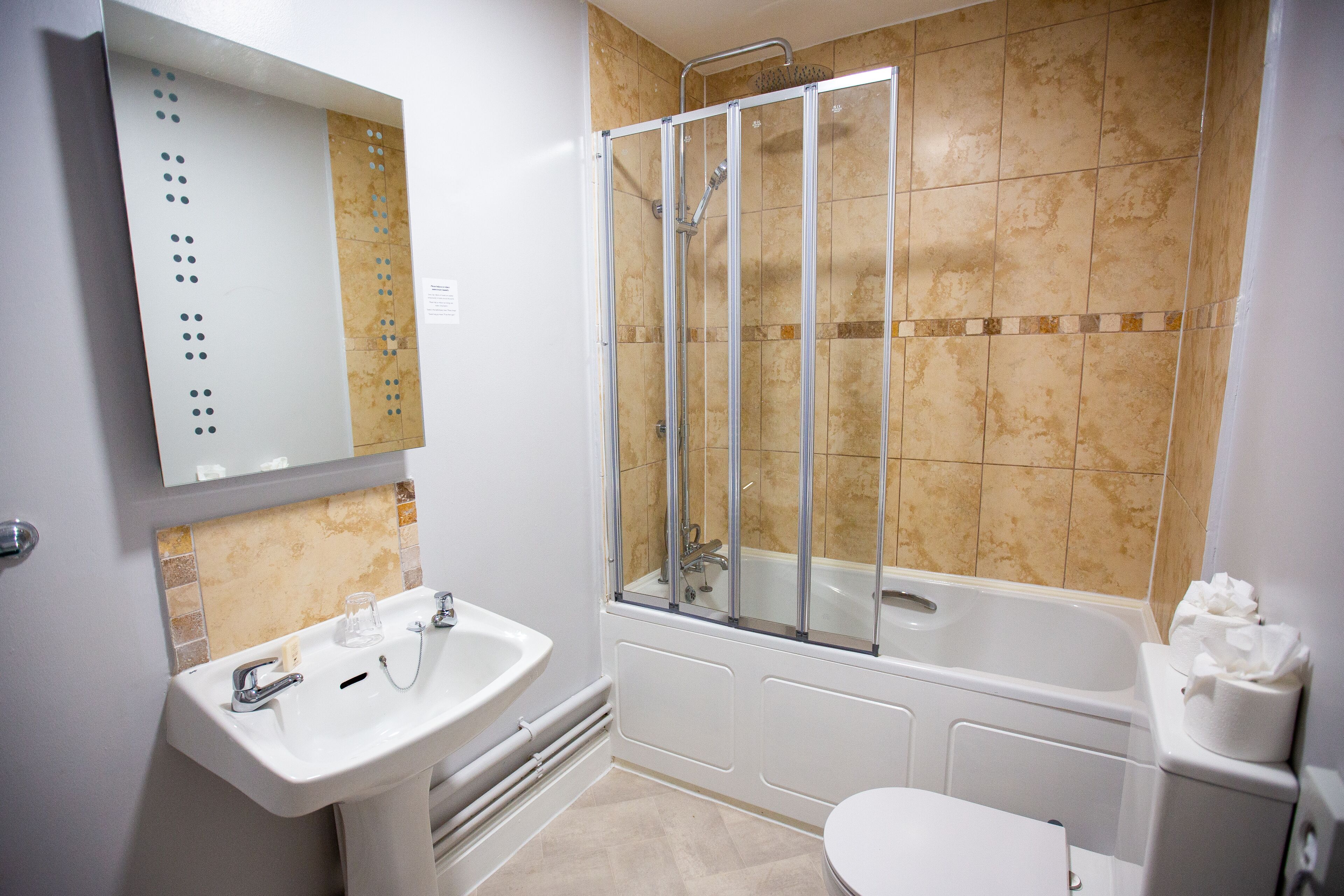 Une salle de bain équipée d’un lavabo, d’un miroir, d’une douche et de toilettes.