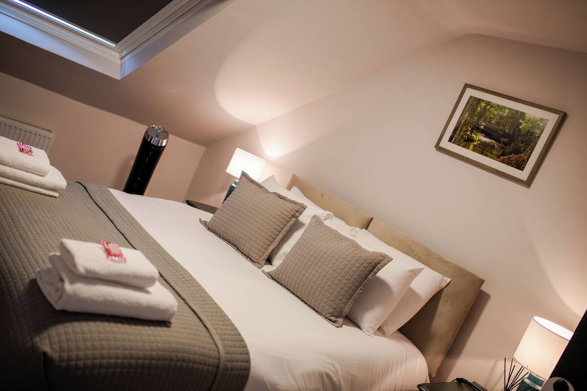 A neatly made bed with pillows and folded towels, a bedside lamp, and a framed picture on the wall.