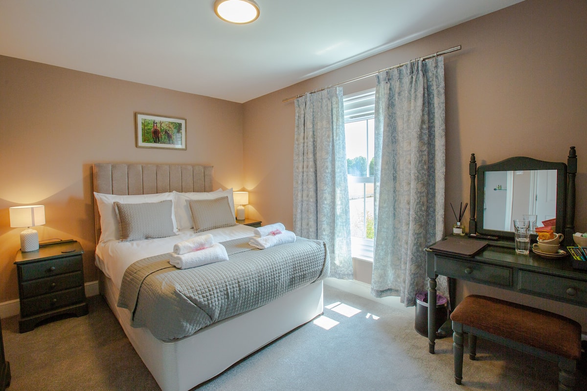 A neatly arranged bedroom with a bed, bedside tables, a desk with a chair, and a window with curtains.