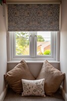 A corner window with a patterned roller blind, two beige pillows, and a small decorative pillow.