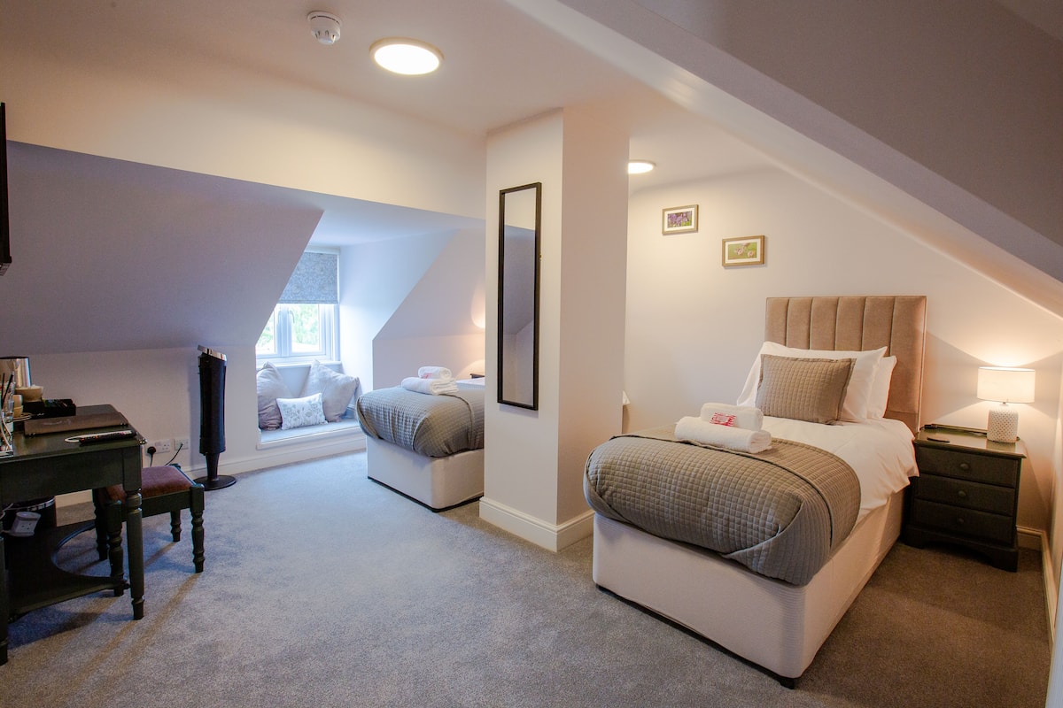 A bedroom with two beds, a desk, and a chair.