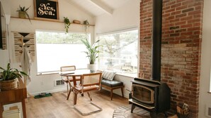 A cozy living room with a brick fireplace, wooden furniture, and large windows. - The Weekender | Hot Tub| Neskowin Village (Neskowin)