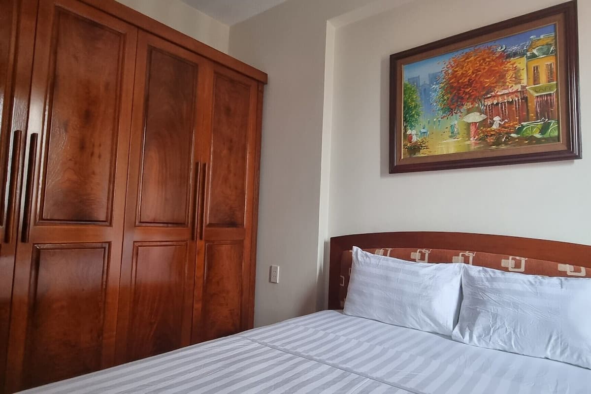 A bedroom with a bed, wooden wardrobe, and a painting on the wall.