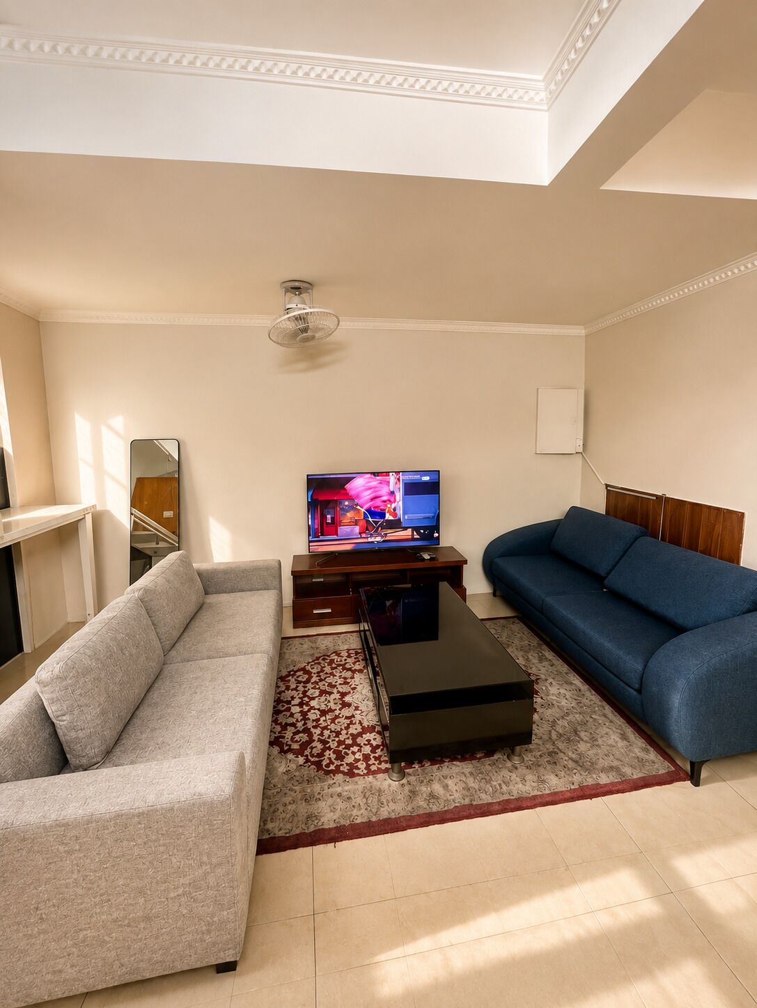 A living room with a sofa, a blue couch, a television, and a ceiling fan.
