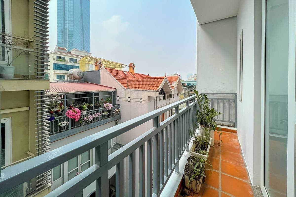 A balcony with a railing, potted plants, and a view of neighboring buildings.