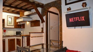 A cozy living area with a glass table and red sofa, a kitchen with wooden cabinets and a microwave, and a door leading to another room. - 3 minutes on foot from Piazza Navona and Castel Sant’Angelo and the Vatican! (Roma)