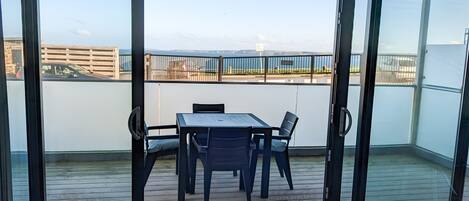 Un balcon avec une table et des chaises, une vue sur une étendue d’eau et, au loin, une chaîne de montagnes.