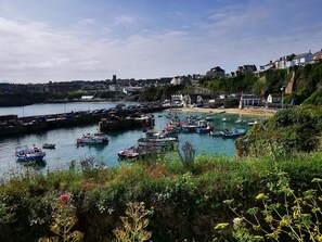 A coastal town with a marina filled with boats, a sandy beach, and buildings along the cliffside. - Fistral Pearl (Newquay)