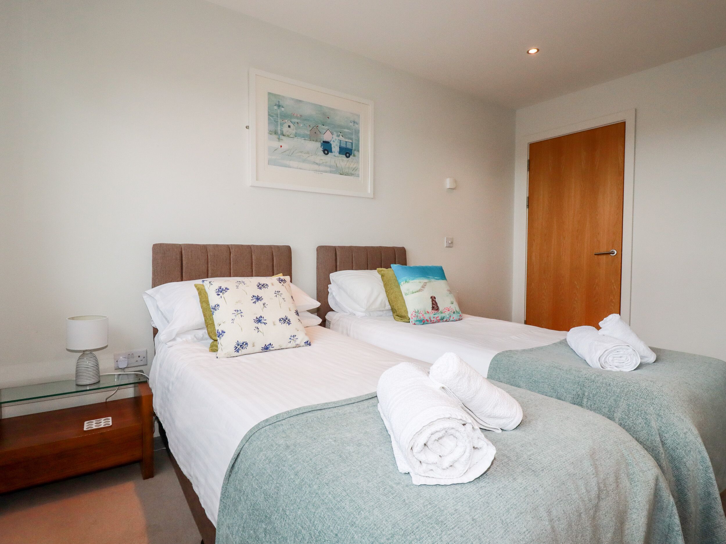 A hotel room with two beds, a nightstand, a lamp, and a painting on the wall.