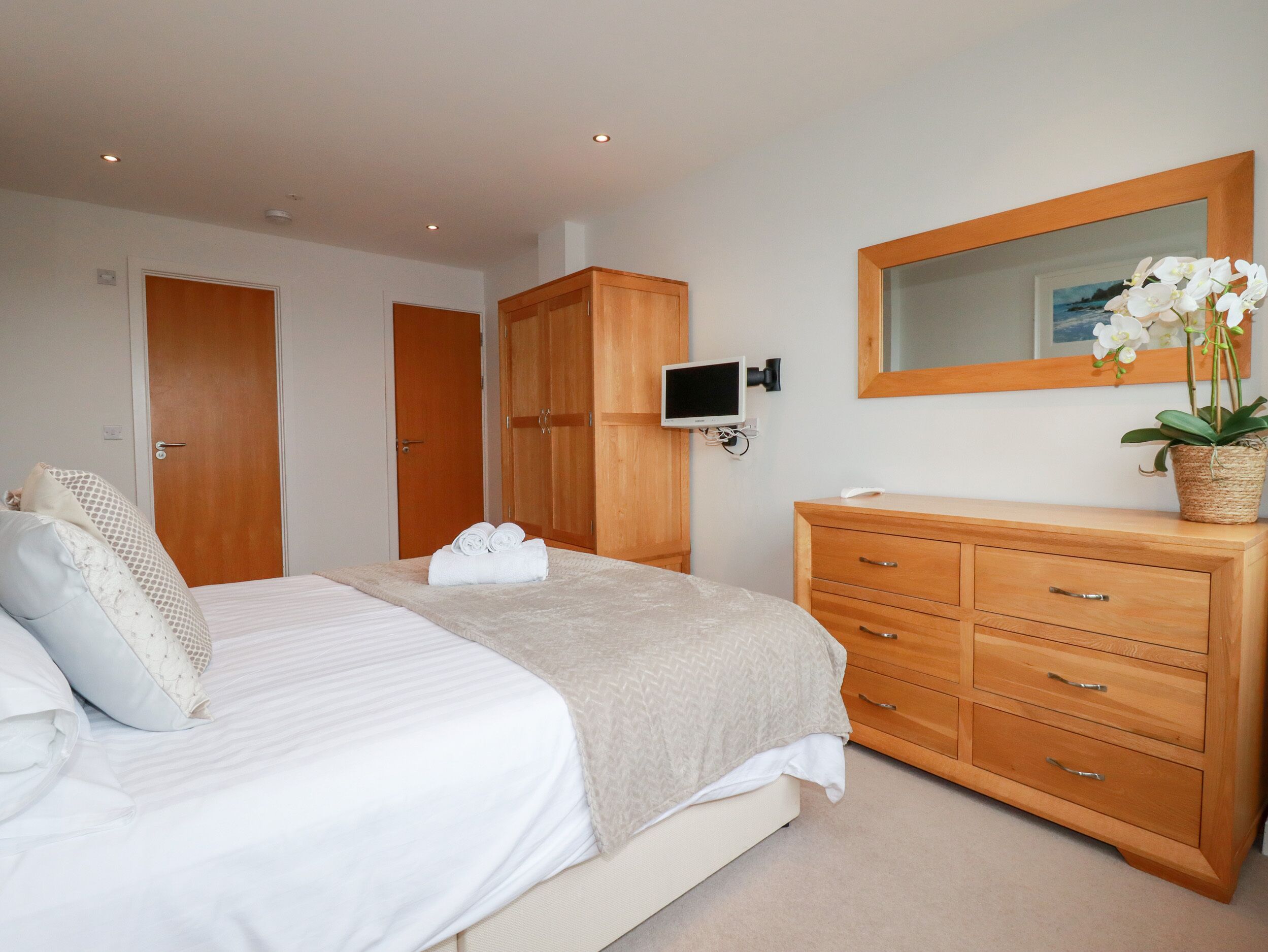 A bedroom with a bed, a wooden wardrobe, a TV, and a mirror.