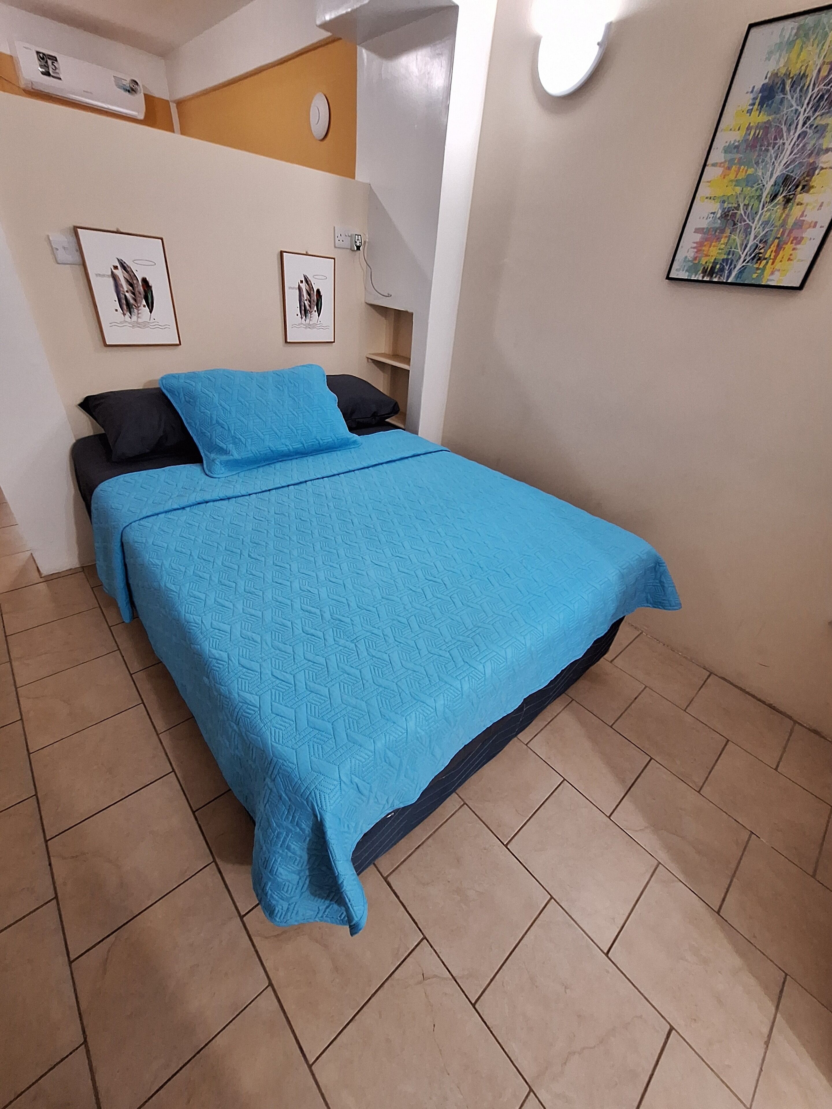 Un lit avec une couvre-lit bleue, deux oreillers noirs et une tête de lit blanche.