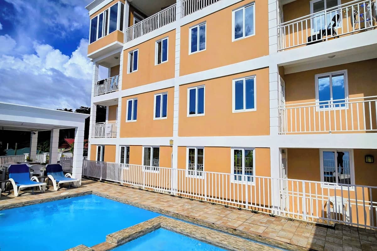 A multi-story hotel with a swimming pool, balconies, and a covered area with lounge chairs.