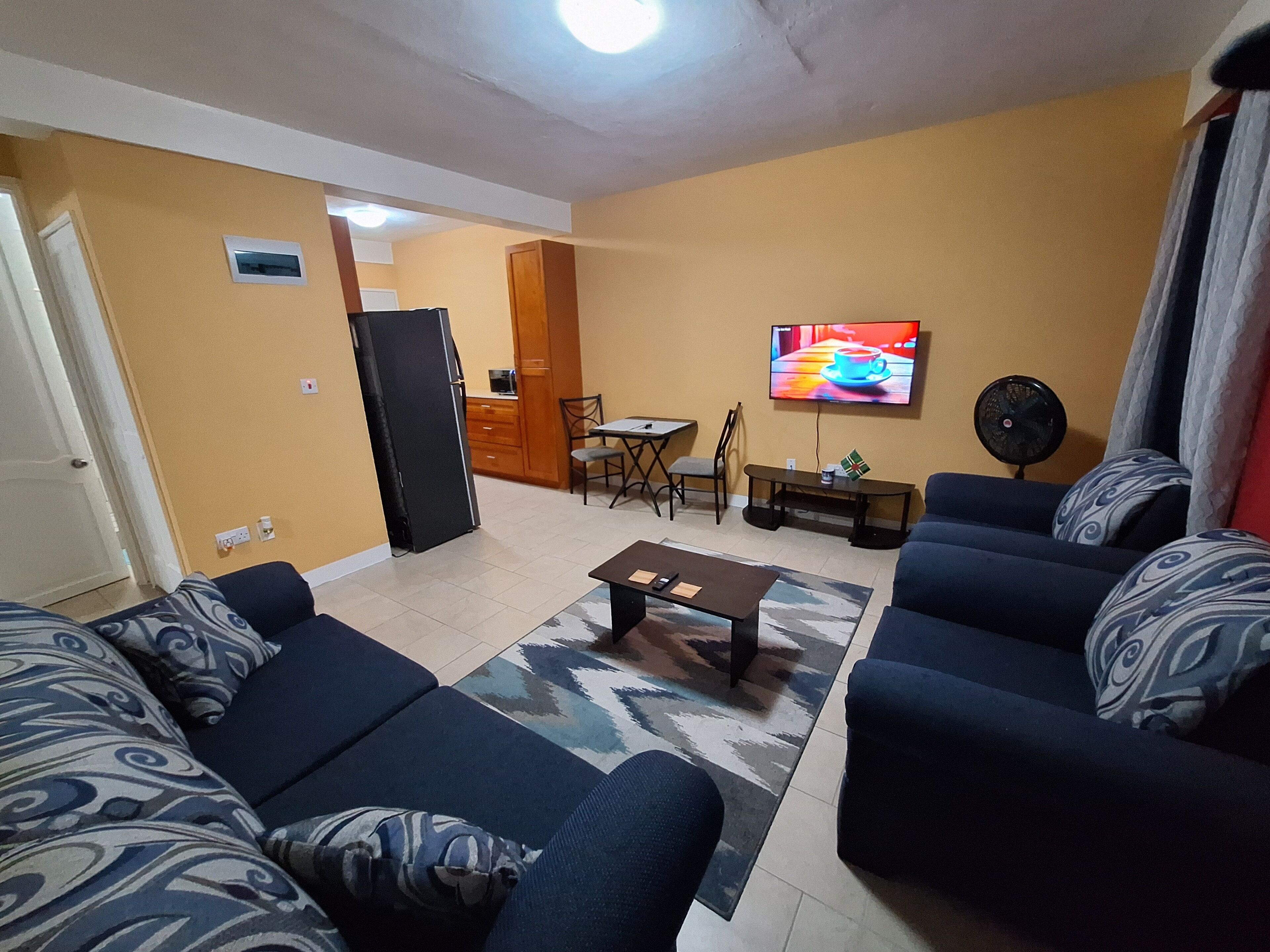A living room with a sofa set, a coffee table, a TV, and a fan.