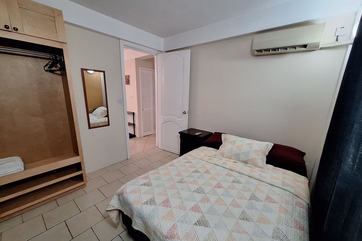 A bedroom with a bed, a wardrobe, a mirror, and an air conditioning unit.