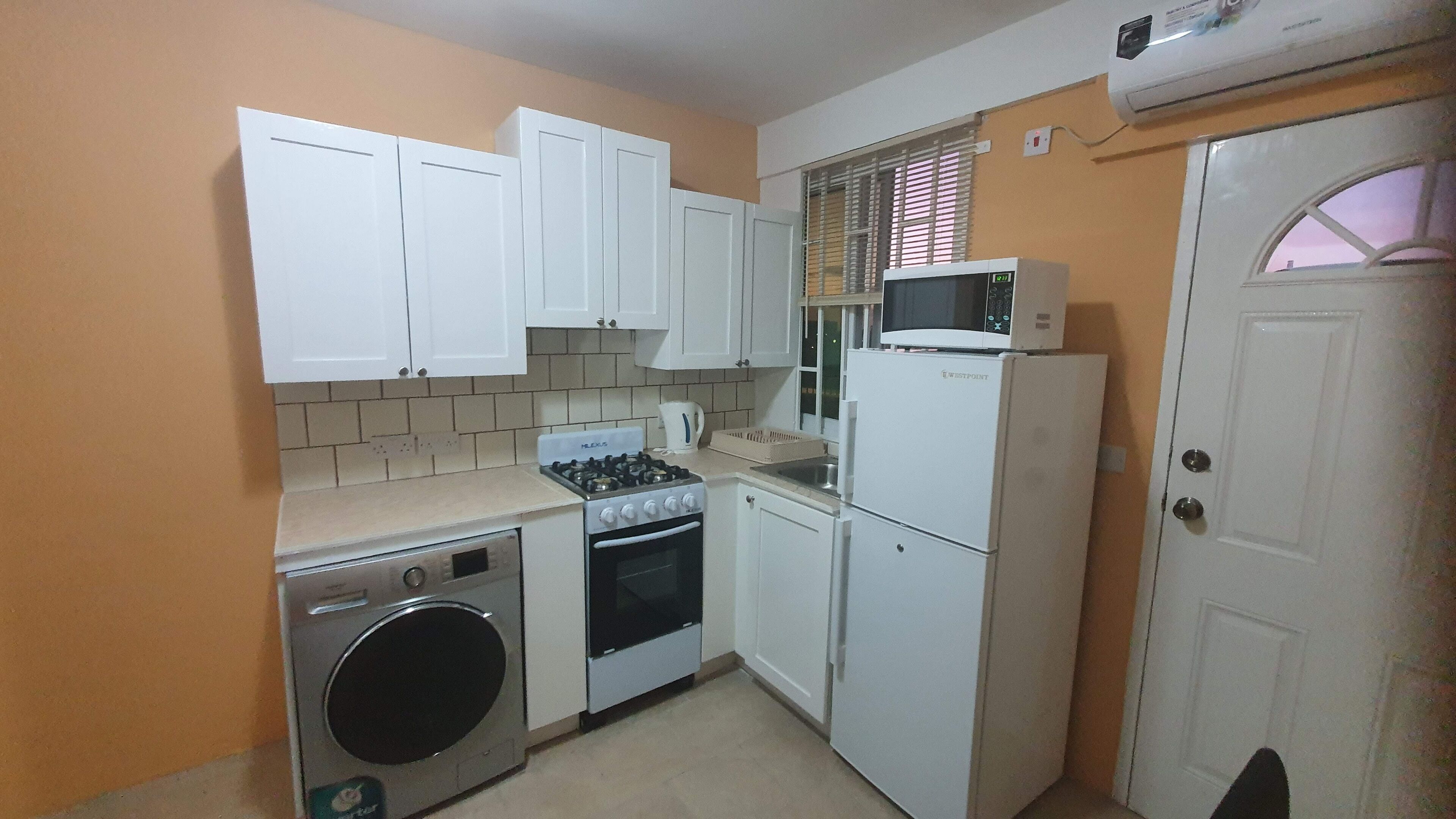 A compact kitchen with white cabinets, a gas stove, a washing machine, a microwave, and a refrigerator.