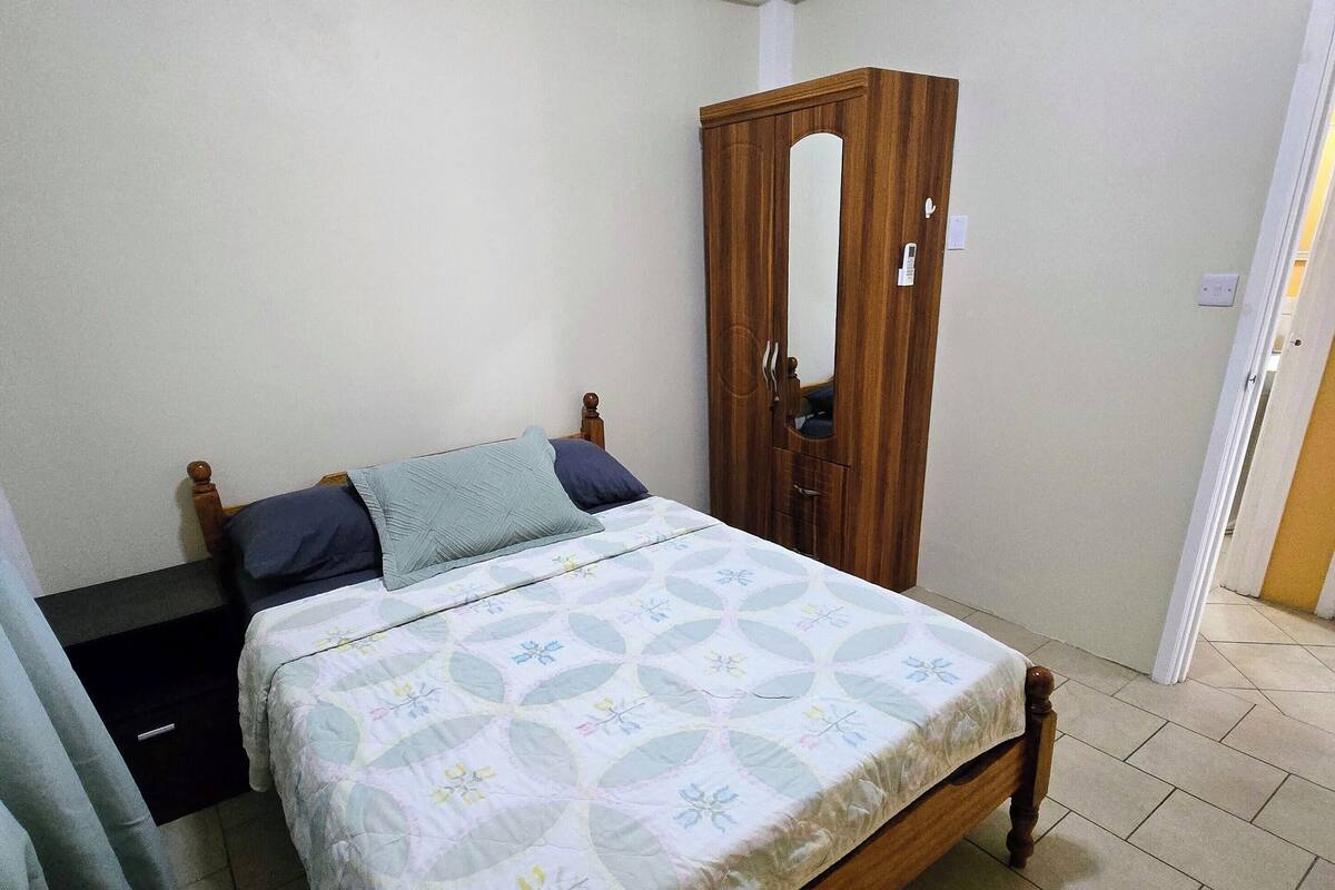 A bedroom with a bed, a wooden wardrobe, a nightstand, and a mirror.