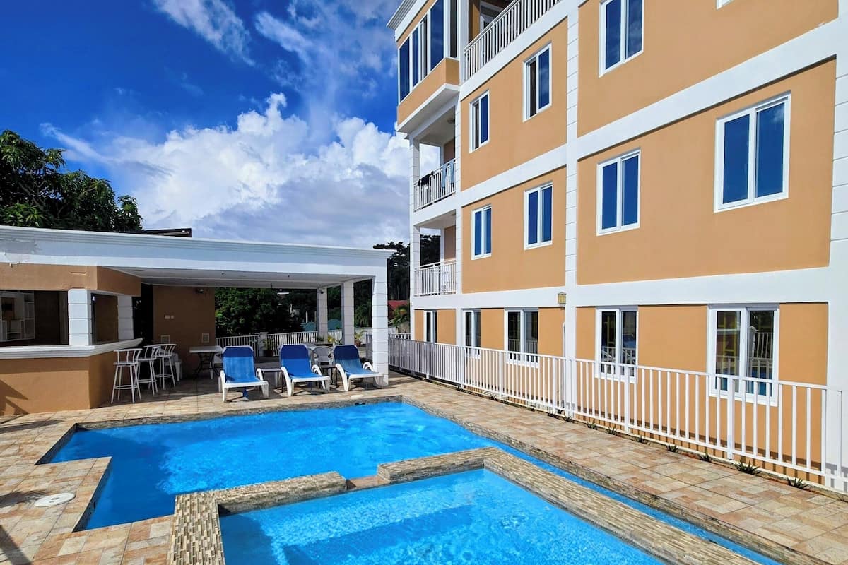 A hotel with a pool area, multiple balconies, and a clear blue sky.