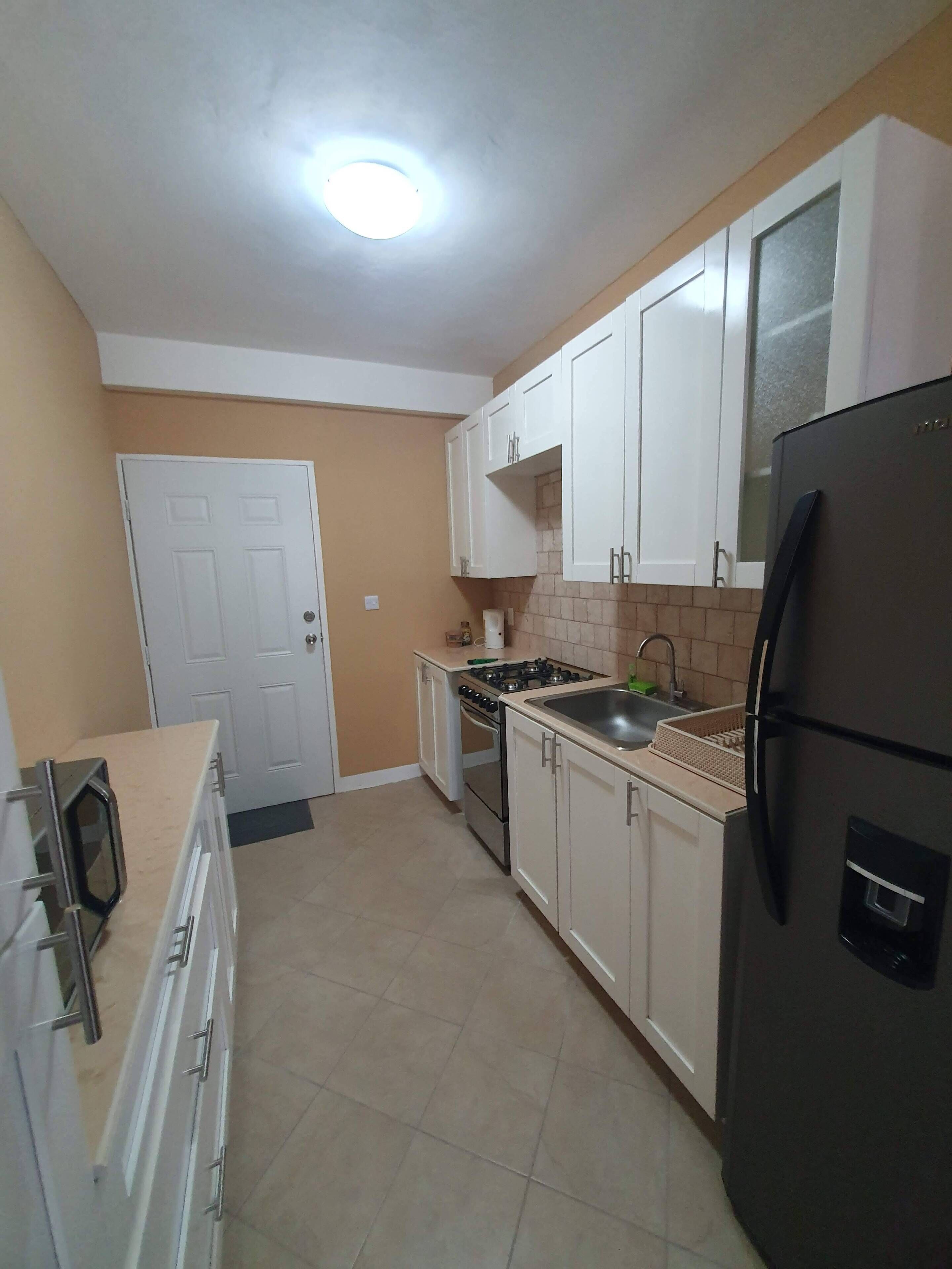 A compact kitchen with white cabinets, a black refrigerator, a stove, and a sink.