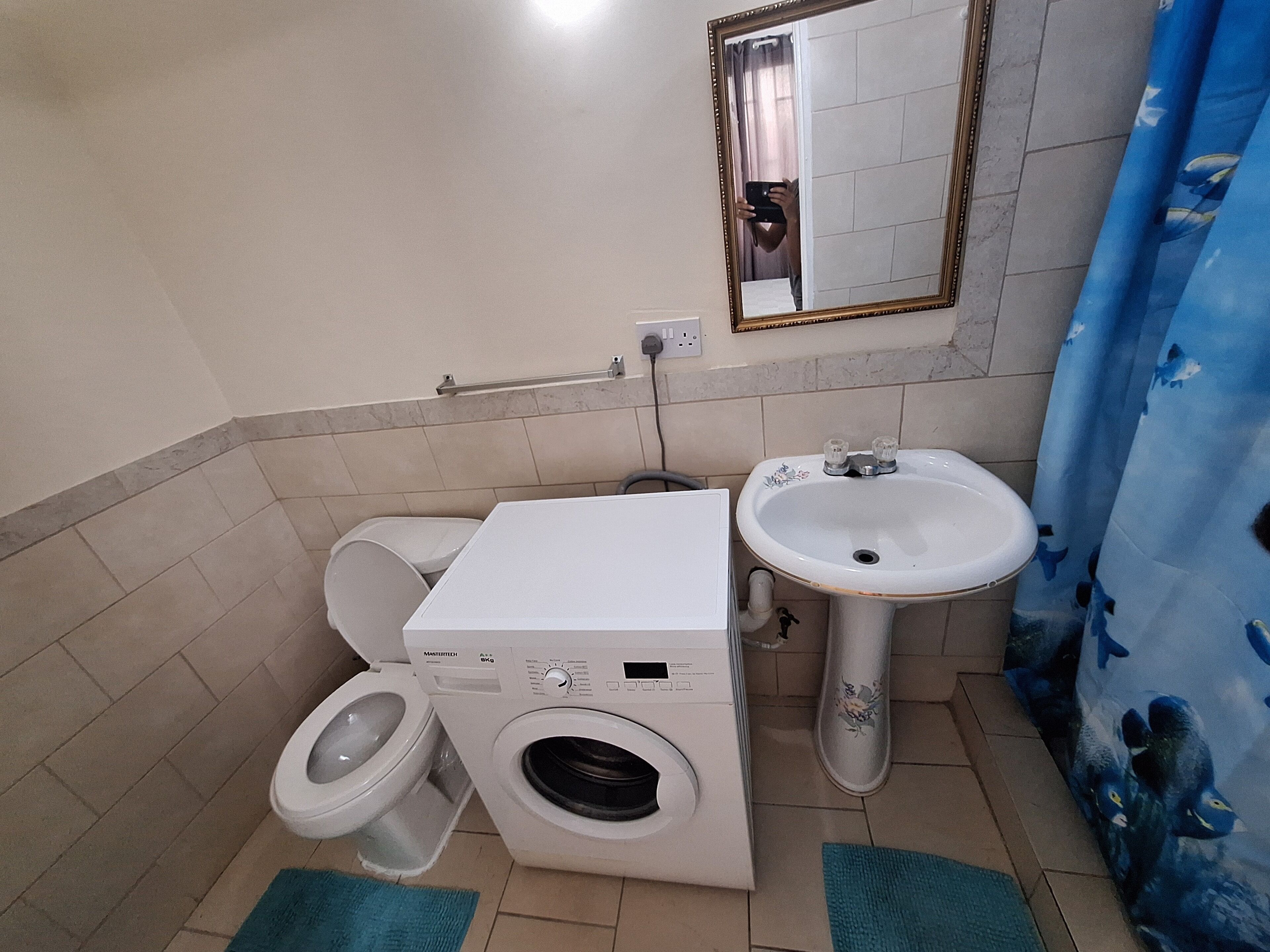 A compact bathroom with a washing machine, toilet, and sink.