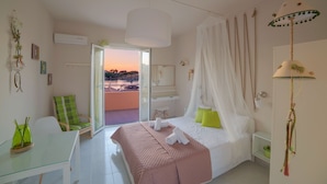 A bedroom with a bed, a chair, a table, and a view of the outside. - Del Mare Beach Hotel (Corfu)