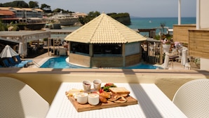 A poolside dining area with a table set for breakfast, overlooking a pool and a view of the sea and buildings. - Del Mare Beach Hotel (Corfu)