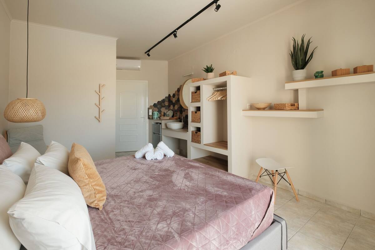 A bedroom with a bed, pillows, a bedside table, a hanging light, a wardrobe, shelves, and a potted plant.