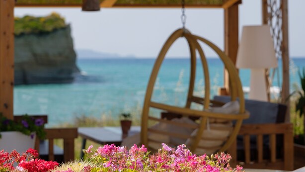 A wooden gazebo with a hanging chair and a table, overlooking a coastal view with a cliff and the sea. - Del Mare Beach Hotel (Corfu)