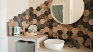 A bathroom with a white sink, a round mirror, and a hexagonal tile backsplash. - Del Mare Beach Hotel (Corfu)