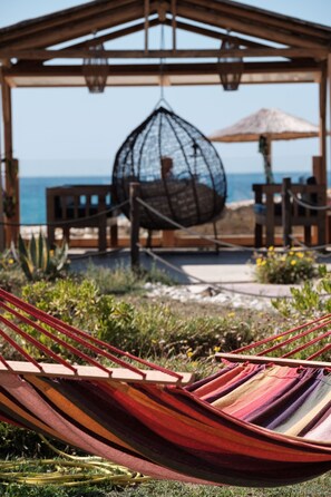 A hammock in a garden area with a wooden pergola and a hanging chair, overlooking a beach. - Del Mare Beach Hotel (Corfu)