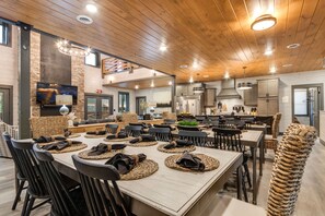 Un vaste espace dédié à la salle à manger, avec une longue table, de nombreuses chaises et un plafond haut orné de poutres en bois.