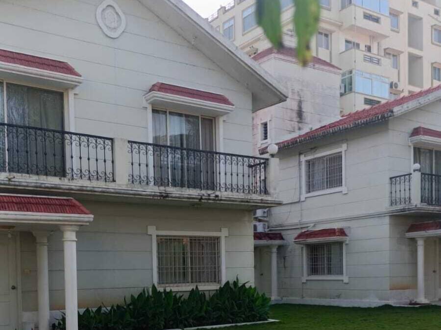 Un edificio residencial de varios pisos con techo plano, paredes exteriores blancas y un pequeño jardín delantero.