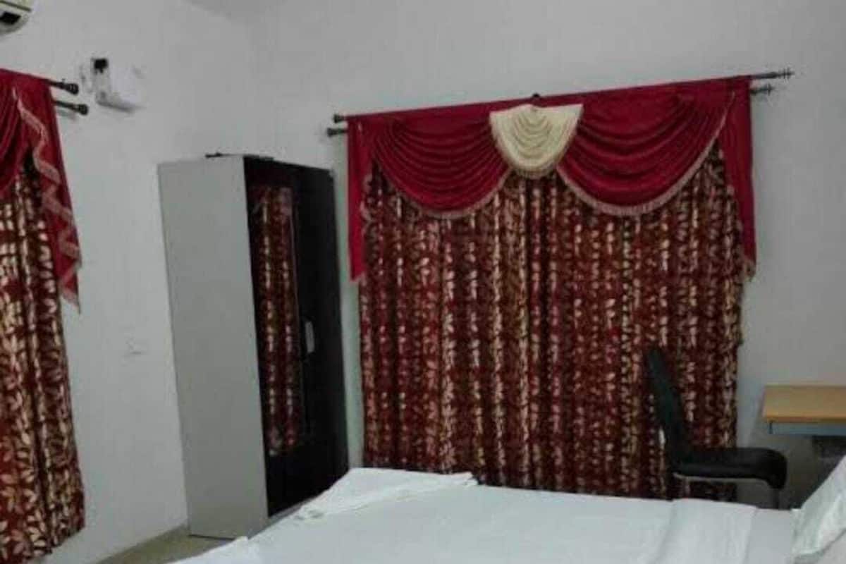 A single-bed room with a white mattress, red curtains, and a black chair.