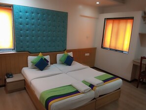 A double bed with a tufted headboard, two bedside tables, and a window with curtains. - Serenity By Monarch Viman Nagar (Pune)