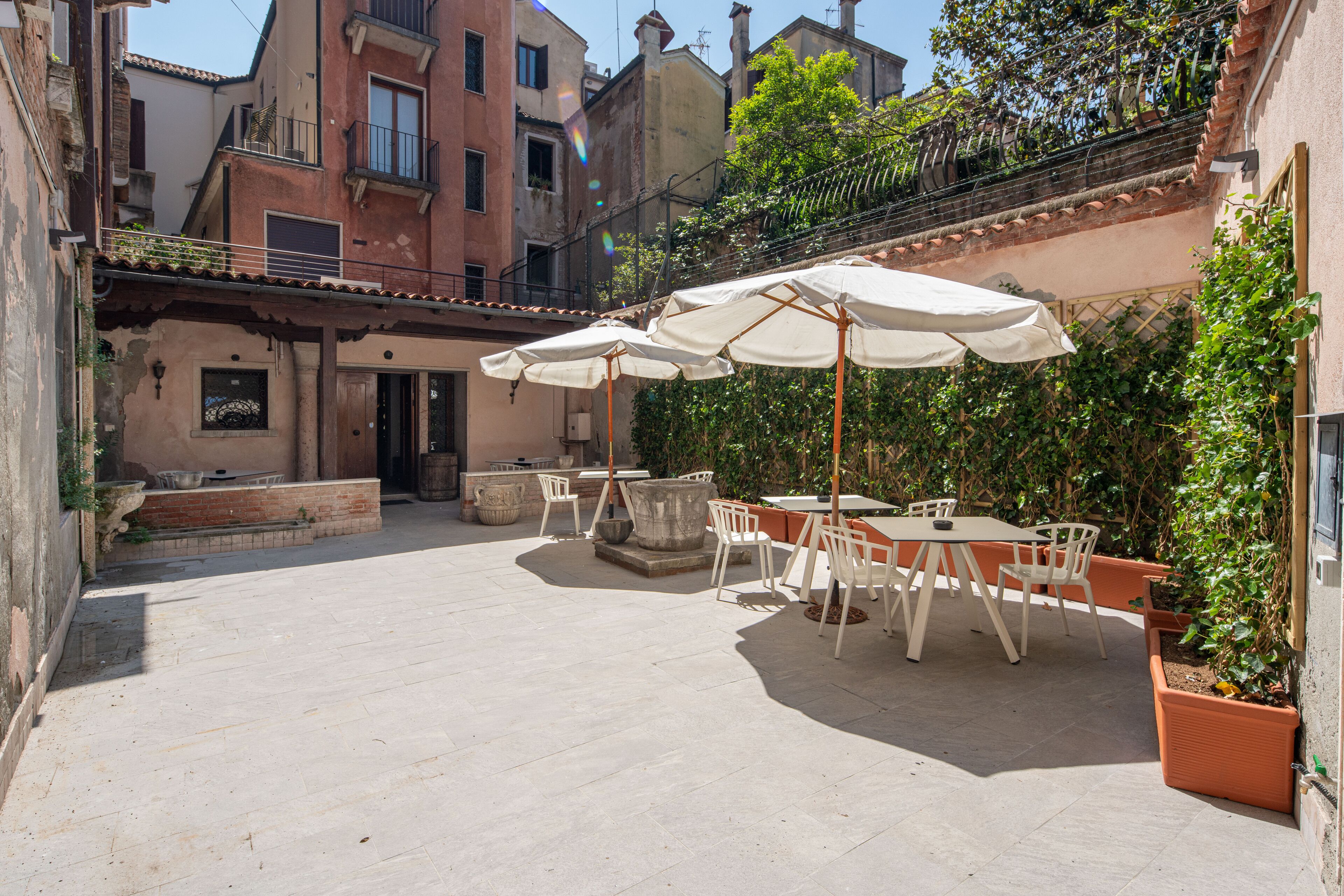 An outdoor patio area with tables and chairs, surrounded by buildings and greenery.