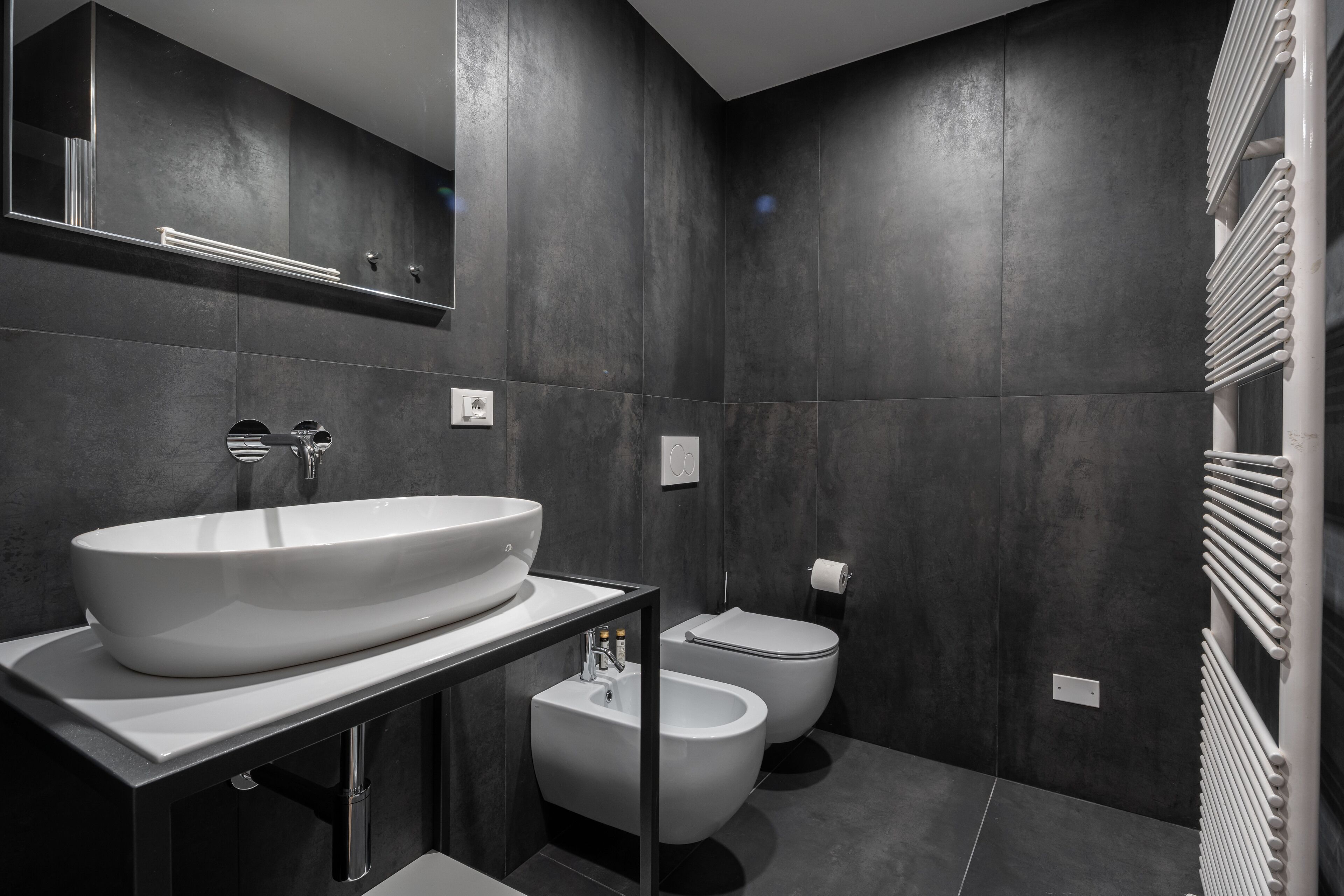 A modern bathroom with a large white sink, a bidet, and a toilet.