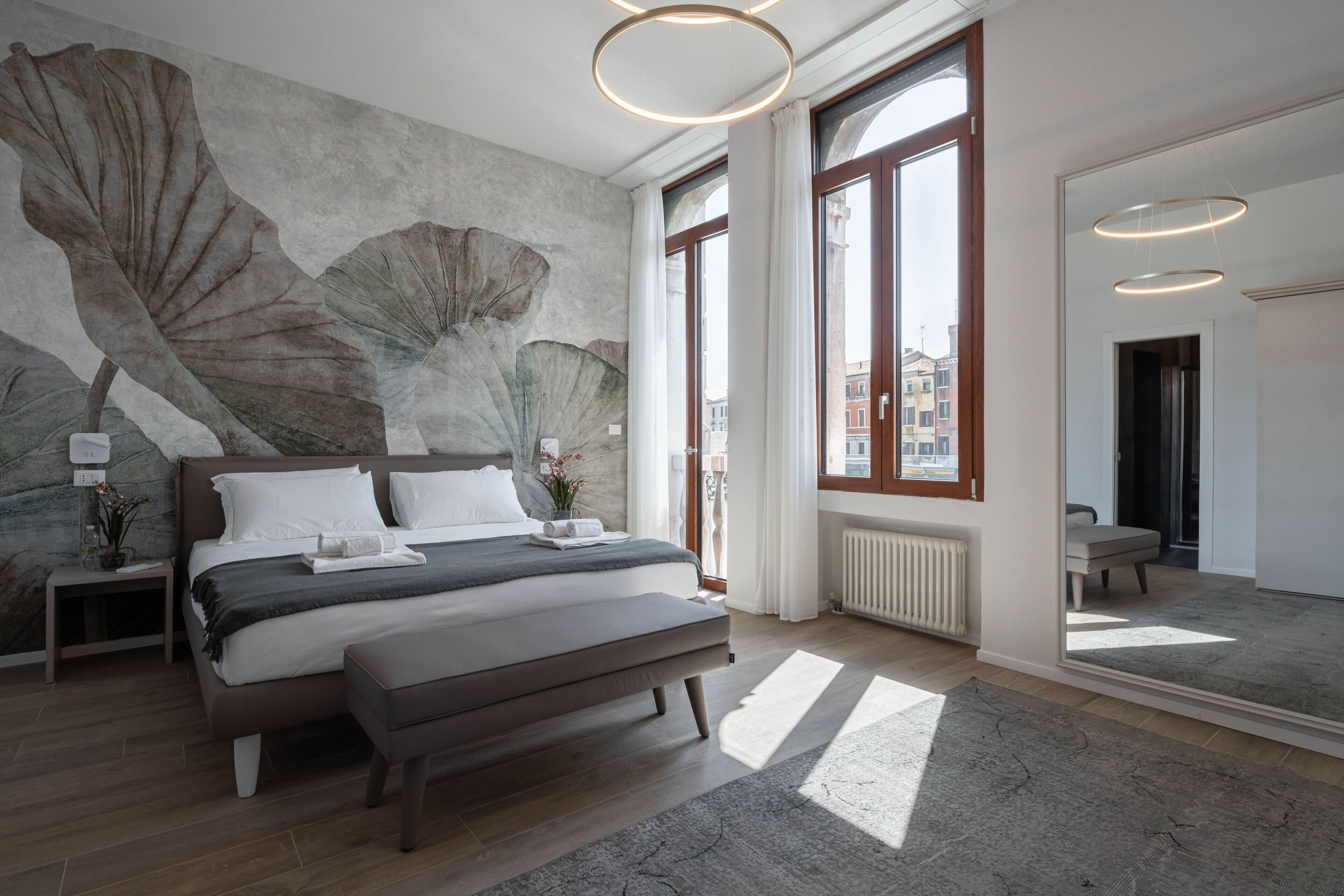 A modern bedroom with a large bed, a wall mural, and large windows.