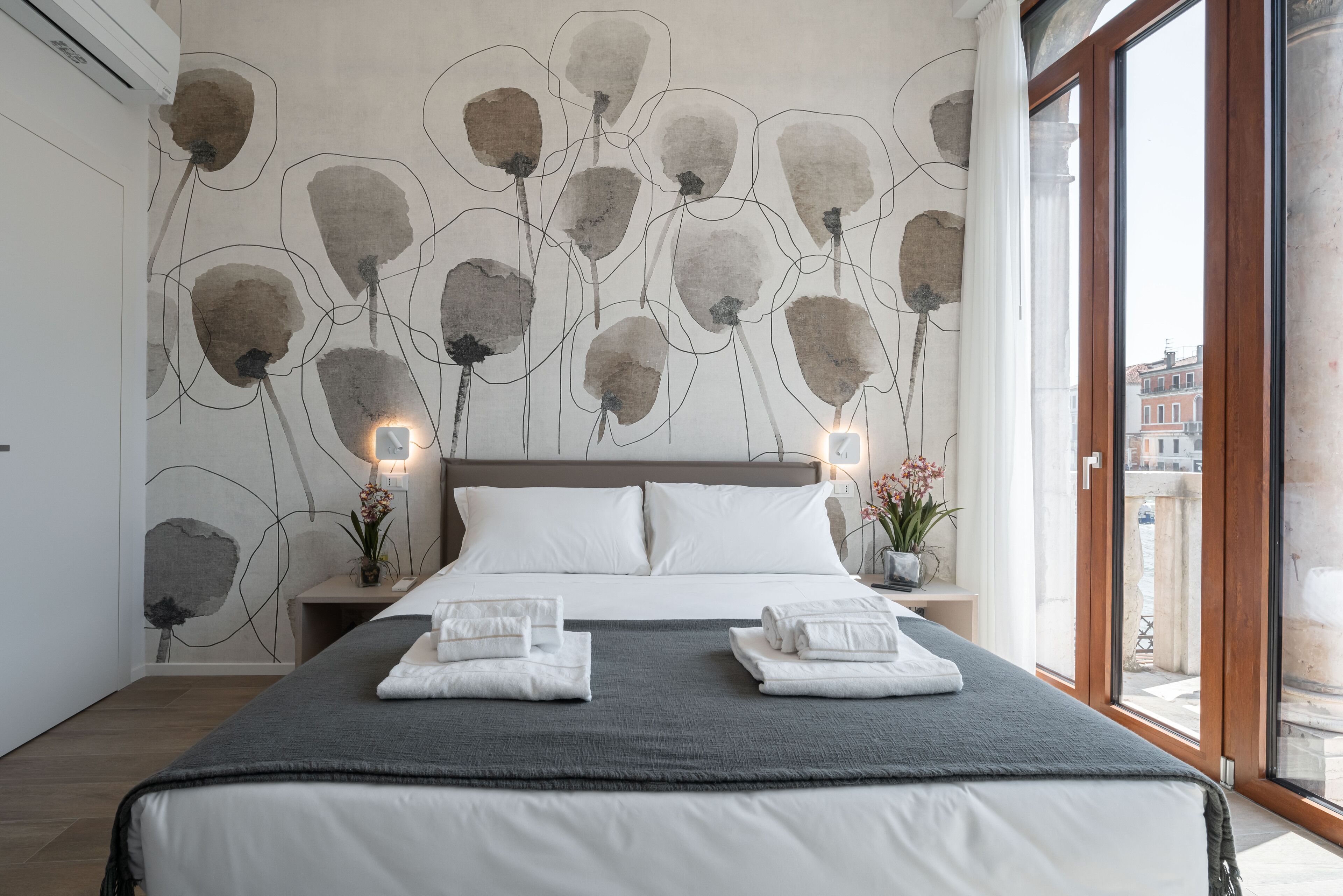 A modern hotel room with a large bed, a view through a glass door, and a wall with abstract art.