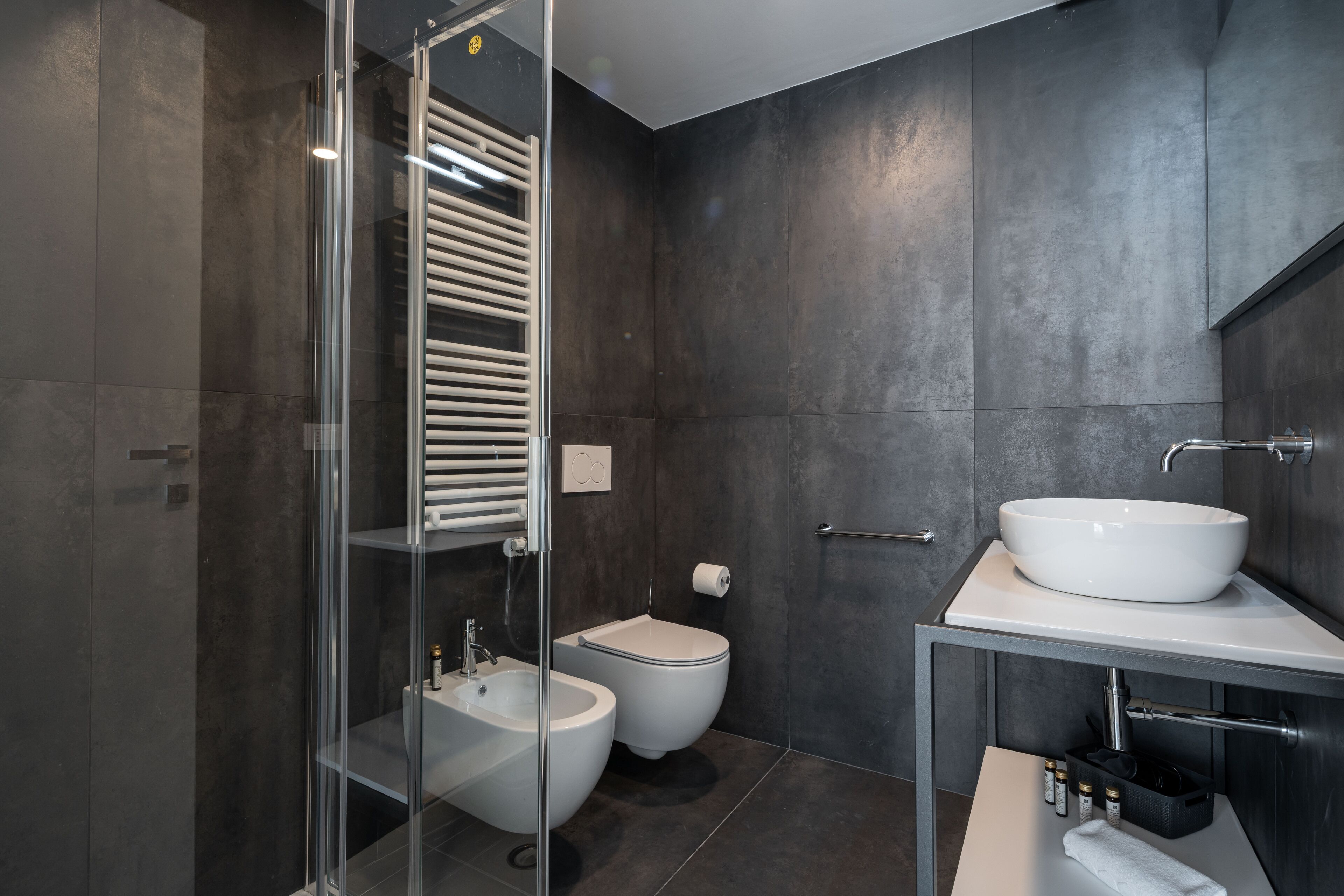 A modern bathroom with a glass-enclosed shower, a bidet, a toilet, and a vanity with a sink and mirror.