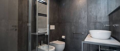 A modern bathroom with a glass-enclosed shower, a bidet, a toilet, and a vanity with a sink and mirror.