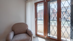 A room with a beige armchair, a large sliding glass door, and a view of a canal and buildings. - Palace Canal View by Wonderful Italy (Venice)