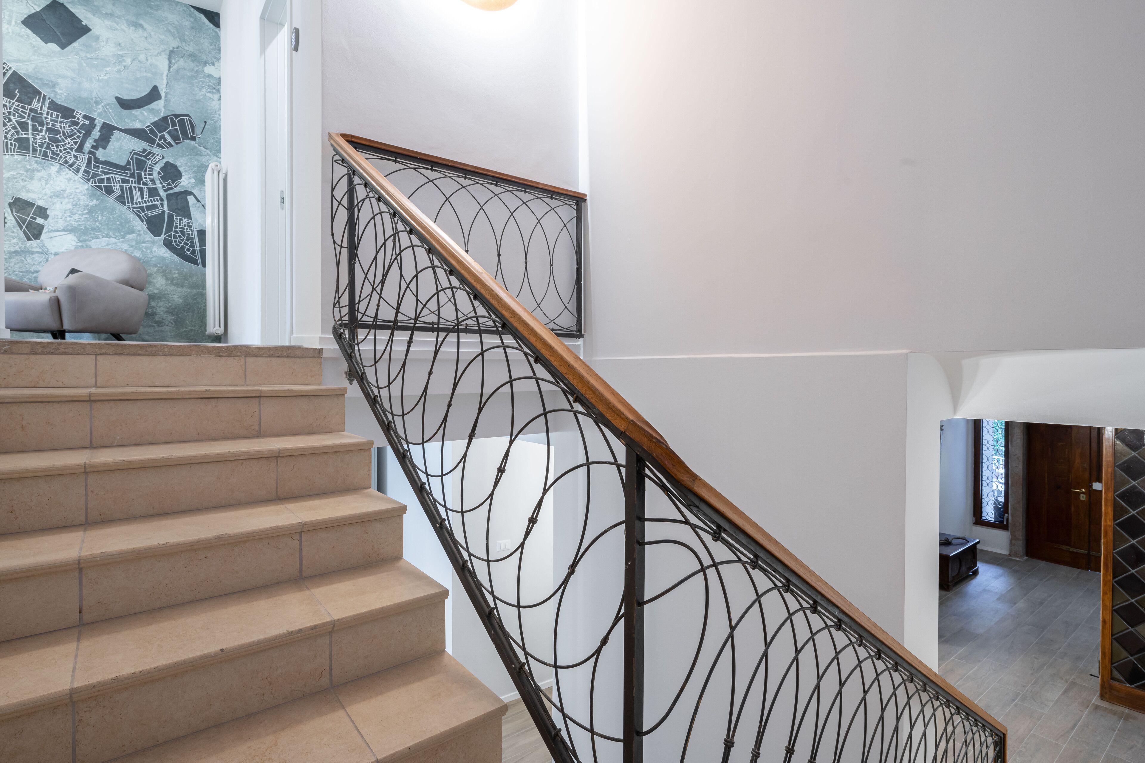 A staircase with a wooden handrail and a metal balustrade, leading to a room with a white wall and a map mural.